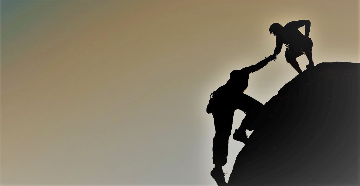 A person atop a mountain helping another person reach the top.