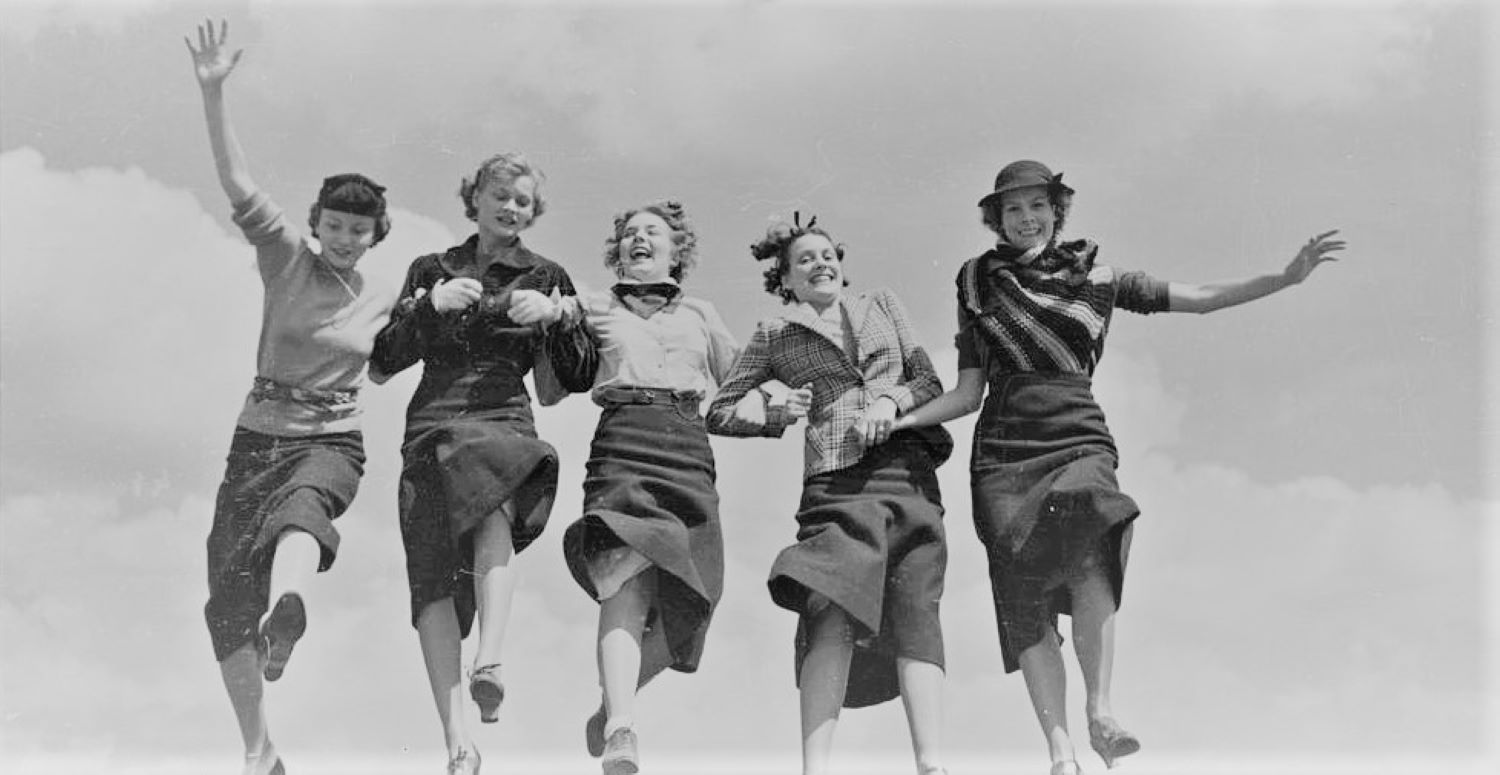 Five women holding hands and walking together in a row.